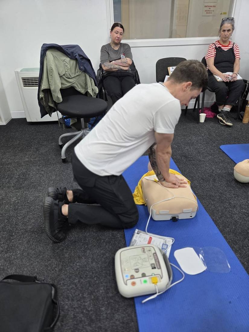 First aid trainer demonstrating an AED defibrillator and CPR on a manikin to delegates during on-site training