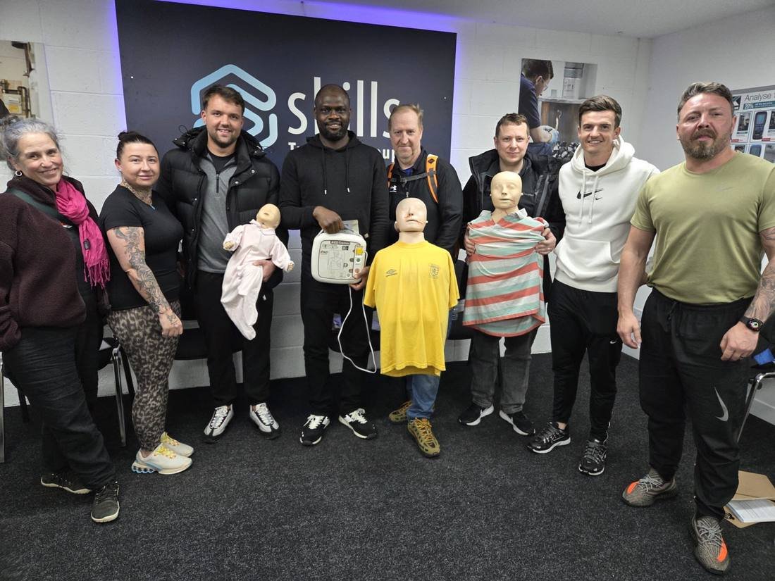 Group of delegates holding training manikins after an on-site first aid course with Skills Training Group